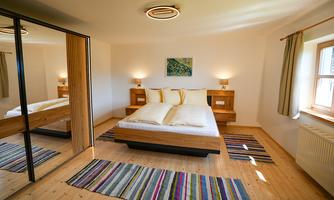 A modern bedroom with a large bed and stylish wooden furniture. The room is bright and inviting, with colorful rugs and a mirrored front.