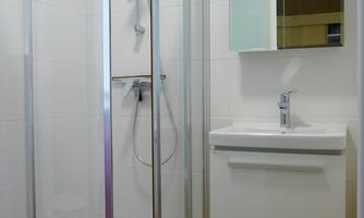 A modern bathroom with a shower cubicle and a vanity. The walls are tiled in light colors and the floor is equipped with tiles.