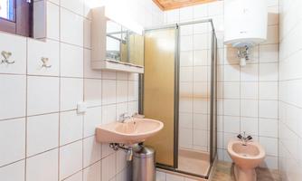 A modern bathroom with a shower area and a sink installation. The walls are clad with white tiles, and there is a wooden ceiling area.