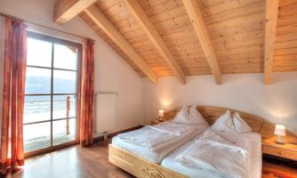 A cozy bedroom with a wooden ceiling and two single beds. Large windows provide a view and plenty of light.