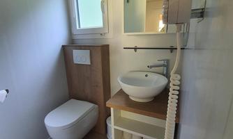 A modern bathroom with a toilet and a sink on a wooden countertop. There is a large window that lets in natural light.