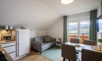 A modern apartment with a bright seating area and a dining table. Large windows offer a beautiful view of the mountains.