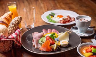 A hearty breakfast with sausage, cheese, fresh vegetables, and an egg. There are also rolls, fruit, and drinks.