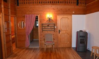 A cozy room with wooden walls and a wooden floor. There is a door, a chair, and a cozy corner with a lamp.