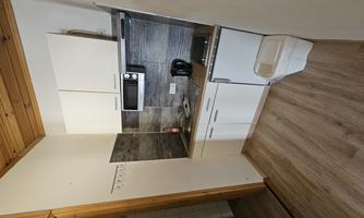 A small kitchen with white cabinets and modern appliances. The room has a wooden floor and a simple wall design.
