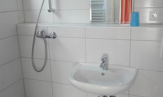 A modern bathroom with a shower and a small sink. The walls are tiled in white and the floor has a blue tile.