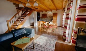A cozy living space with a sofa and a dining table. The wooden ceiling and large windows create a bright atmosphere.