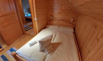 A cozy wooden bedroom with a double bed. The walls and furniture are in warm wood tones, and there are soft pillows on the bed.