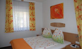 A cozy bedroom with a double bed and colorful curtains. The walls are decorated with a cheerful piece of artwork.
