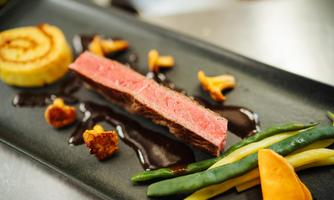An elegantly arranged plate with perfectly cooked meat, colorful vegetables, and a dark sauce. Accompanied by a spiral-shaped side dish.