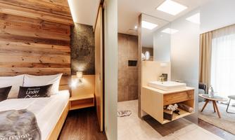 A modern bedroom with wood paneling and a comfortable bed. Next door is an elegant bathroom with modern fixtures and plenty of light.