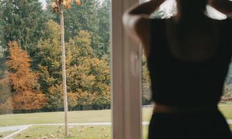A person is training in a room overlooking an autumn garden. Through the window, you can see a tree and colorful leaves.