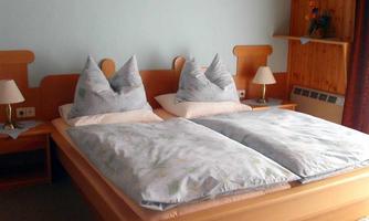 A cozy bedroom with a double bed and white bedding. There are two nightstands with lamps and a warm wooden paneling on the wall.
