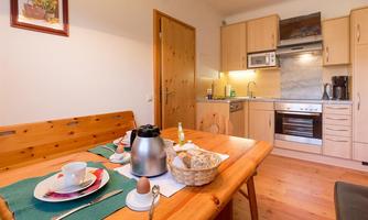 A cozy kitchen with a wooden table and a breakfast set. In the background, modern kitchen cabinets and appliances can be seen.
