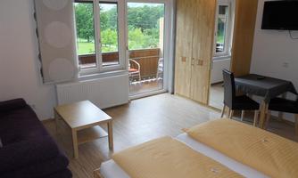 A bright room with two beds, a sofa, and a table. Large windows provide a view of the green landscape outside.