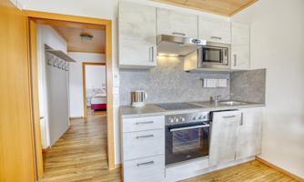 A modern kitchen with white cabinets and a stove. In the background, a hallway is visible, leading to another room.