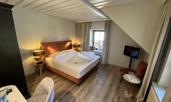 A cozy bedroom with a large bed and warm lamps. The room has wooden flooring and a small television.