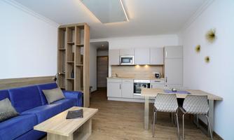 A modern apartment kitchen with a blue sofa and a dining table. The room is bright and cheerfully designed.