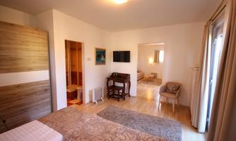 A cozy bedroom with a double bed and a small table. The room is bright and modernly designed, with access to another room.