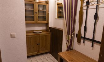 A bright entrance area with tiles and wooden shelves. Coat hooks hang on the wall and a curtain in purple stripes.
