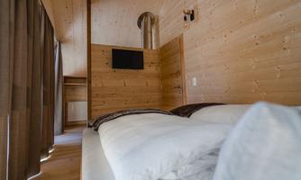 A bright and cozy sleeping room with wooden paneling. The room features a bed, a television, and curtains.