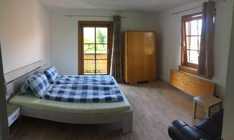 A simple bedroom with a large double bed and checkered bedspreads. The room has large windows that let in plenty of daylight.