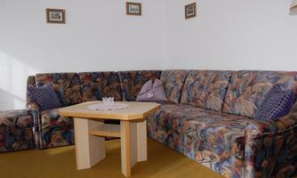 A cozy living room with a colorful couch and a wooden table. Small pictures are hanging on the walls.