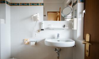 A simple bathroom with a sink, a mirror, and a towel rack. The walls are brightly tiled and there is a door that leads to another room.
