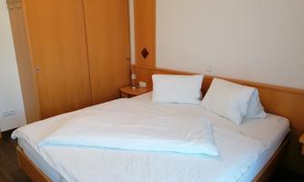 A cozy bedroom with a large bed and wooden cabinets. The walls are bright, and the room feels inviting and calm.