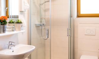 A modern bathroom with a glass shower and a sink. There is a large mirror and a bright window opening.