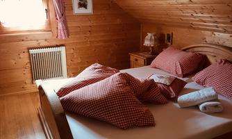 A cozy bedroom with wooden walls and a large double bed. Red pillows and windows with curtains create an inviting atmosphere.