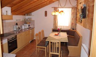 A cozy kitchen with wooden shelves and a dining table. The room has a rustic style and plenty of daylight.