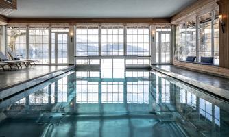 An elegant indoor pool with large windows overlooking a tranquil landscape. There are loungers on both sides of the pool for relaxation.