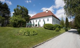 A picturesque building with a red roof, surrounded by green grass and trees.