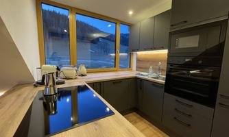 A modern kitchen with a wooden workspace and black appliances. Large windows offer a beautiful view of the landscape.