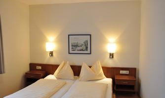 A cozy bedroom with two single beds and gentle wall lamps. A picture hangs on the wall, giving the room a pleasant atmosphere.