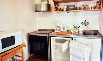 A modern kitchen with a refrigerator, a stove, and a microwave. The shelves are stocked with dishes and kitchen utensils.
