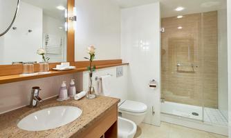 A modern bathroom with a sink, a toilet, and a shower. The design is bright and simple, with a wooden shelf and decorative elements.