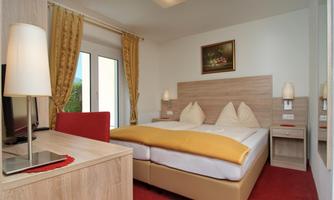 A modern bedroom with a large double bed and pleasant lighting. The windows are decorated with curtains and a desk is present in the room.