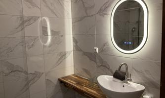 A modern bathroom with bright tiles and an elegant mirror. On the wooden shelf stands a stylish sink.