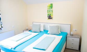 A modern bedroom with a large double bed and bright colors. There are two pillows and fresh bedding in blue and white.