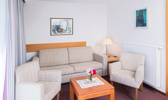 A stylish living space with a beige sofa and two cozy armchairs. On the table, there is a vase with flowers, and the walls are decorated with art pictures.