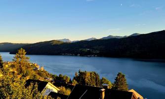 A tranquil landscape with a lake and mountains in the background. The sky is clear and the sun is shining.