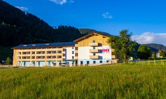 A modern hotel building in a picturesque mountain landscape.  
Surrounded by greenery and blue skies, it offers an inviting atmosphere.