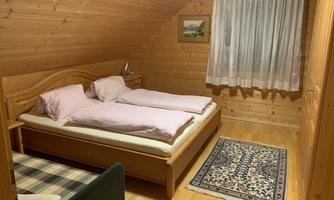A cozy bedroom with wooden paneling. There is a double bed and a soft carpet on the floor.