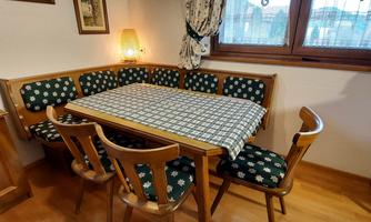 A cozy dining area with a wooden table and a bench. The chairs are upholstered in floral fabric, and the light is warm and inviting.