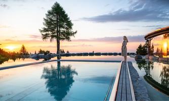 A beautiful pool with a view of the sunset. In the background, there are trees and a relaxing atmosphere.