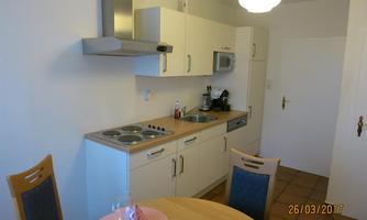 A modern kitchen with white cabinets and a round table. There is a stove, a sink, and some kitchen appliances.