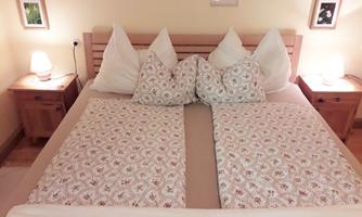 A cozy bedroom with a double bed and four pillows. Next to the bed, there are two bedside tables with lamps.