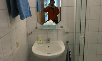 A simple bathroom with a shower, a sink, and towels. A mirror reflects the person taking the photo.
